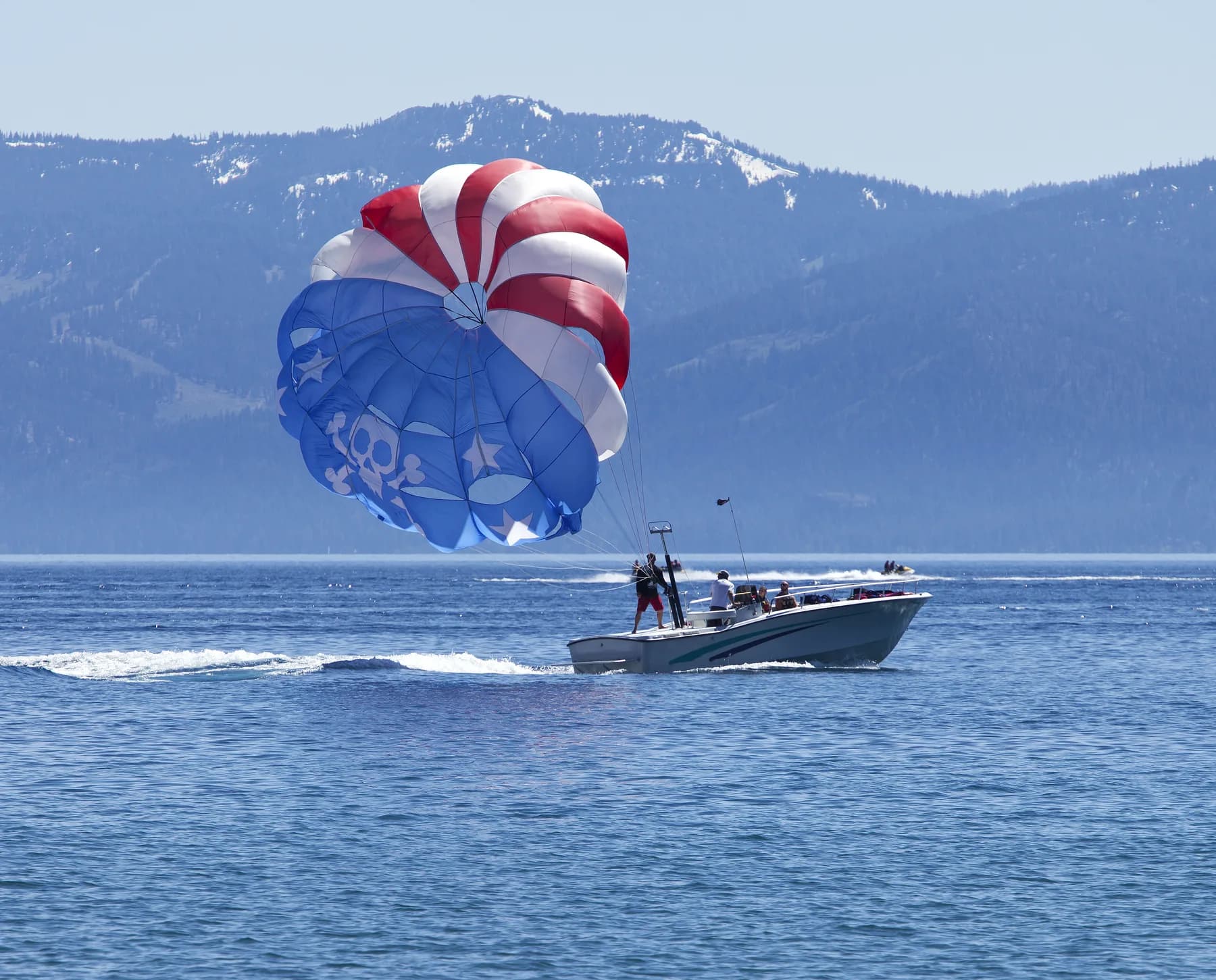 Un parapente rojo, blanco y azul remolcado por una lancha en un lago de montaña