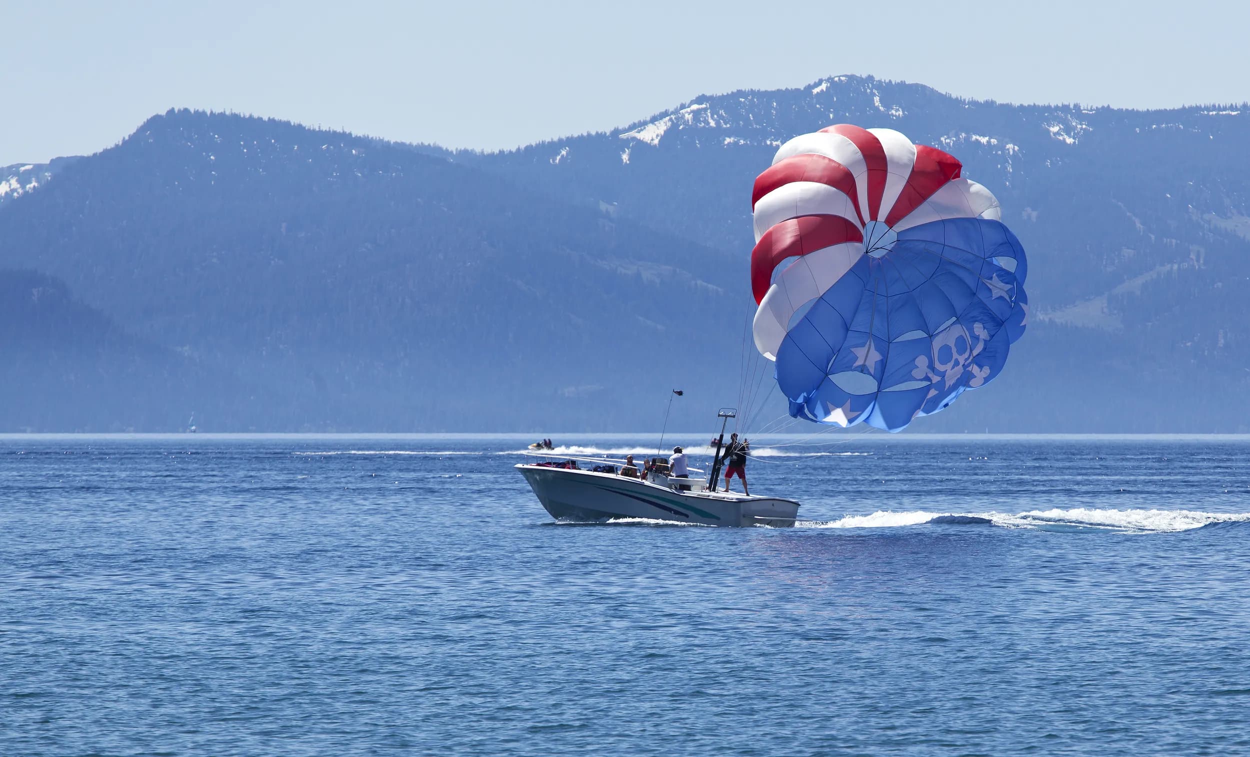 Un parapente rojo, blanco y azul remolcado por una lancha en un lago de montaña