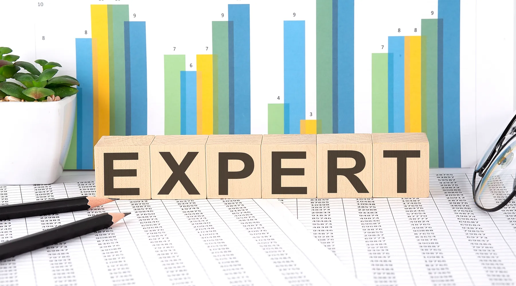 Bloques de madera que forman la palabra EXPERT frente a gráficas del mercado