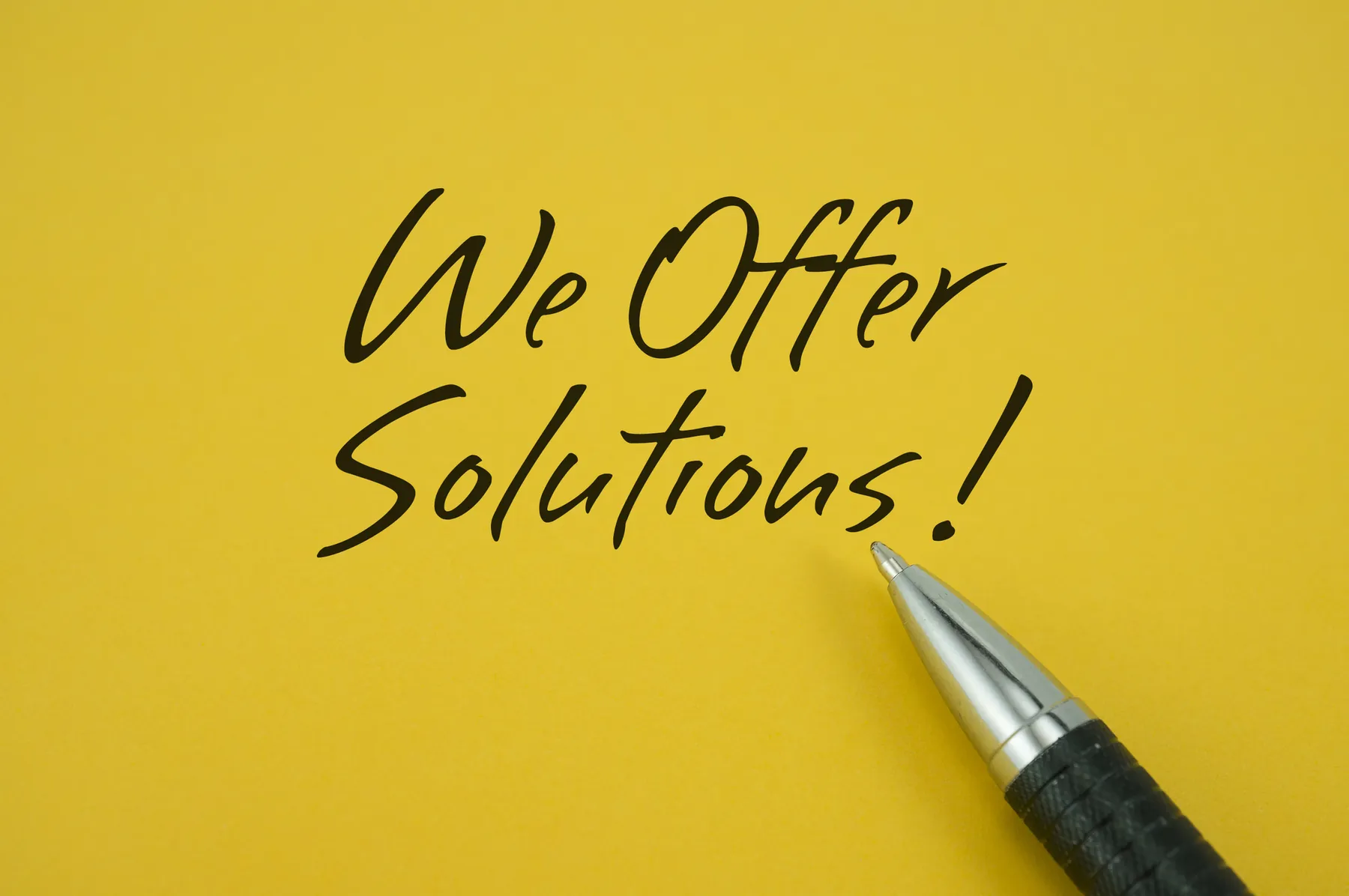 “We Offer Solutions!” escrito a mano en papel amarillo, con una pluma